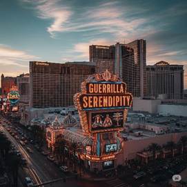 A nighttime view of the Las Vegas Strip featuring a bright marquee sign that reads 'GUERRILLA SERENDIPITY', surrounded by illuminated buildings and a bustling street.