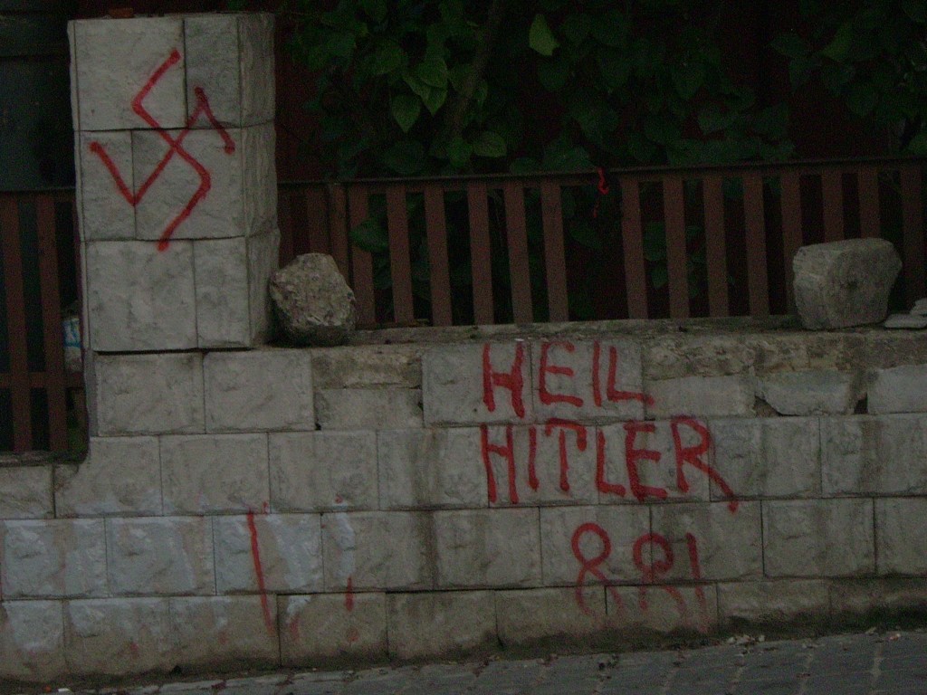 A stone wall featuring graffiti, including a swastika symbol and the phrase 'HEIL HITLER' written in red paint.